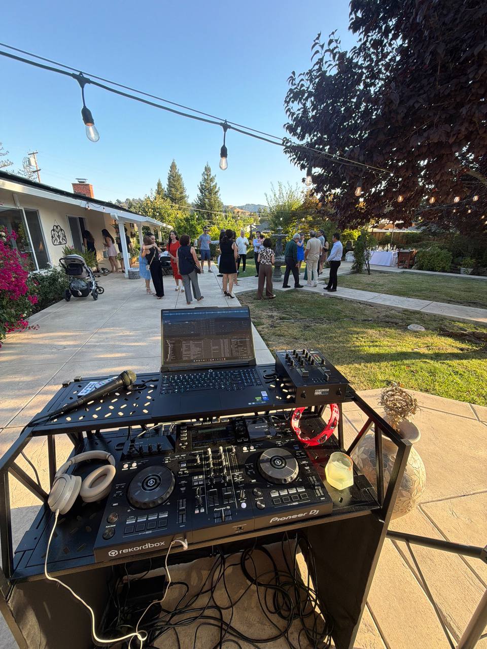 DJ Alphire's booth set up under string lights with guests mingling on the patio at a backyard get-together