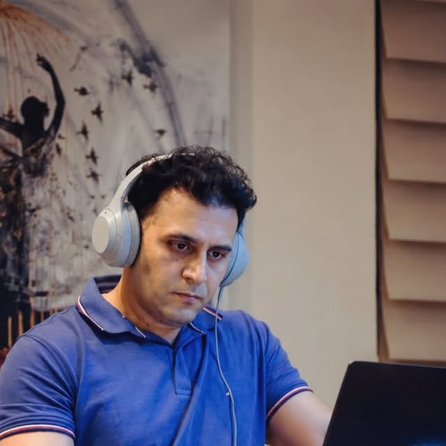 DJ Alphire wearing headphones, working on a laptop at home