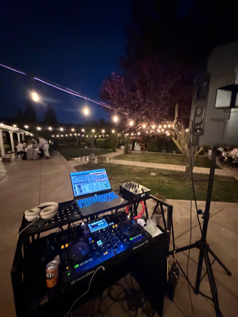 DJ Alphire's controller lit up blue at night with string lights glowing across the backyard