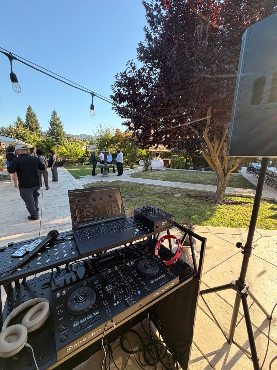 Guests walking past DJ Alphire's booth at golden hour during a backyard celebration