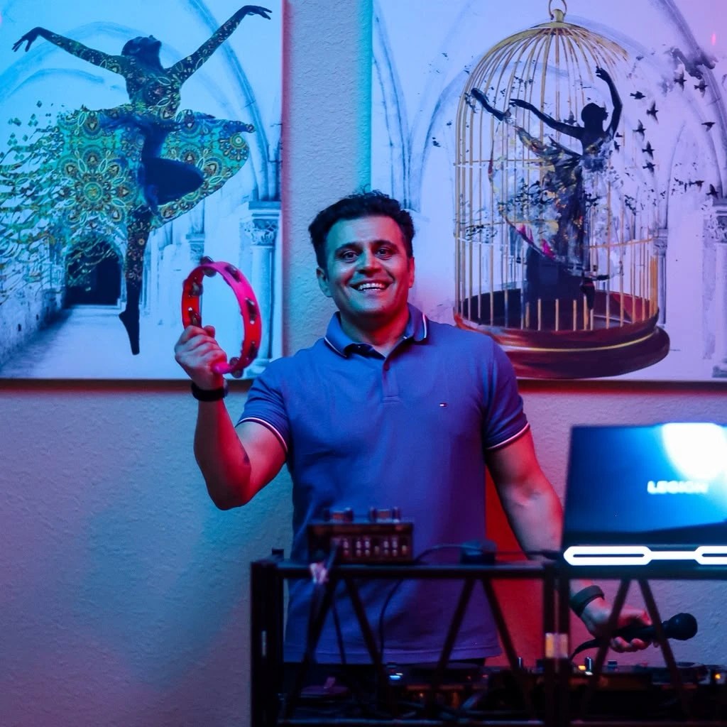 DJ Alphire with a tambourine at the DJ booth under neon lighting