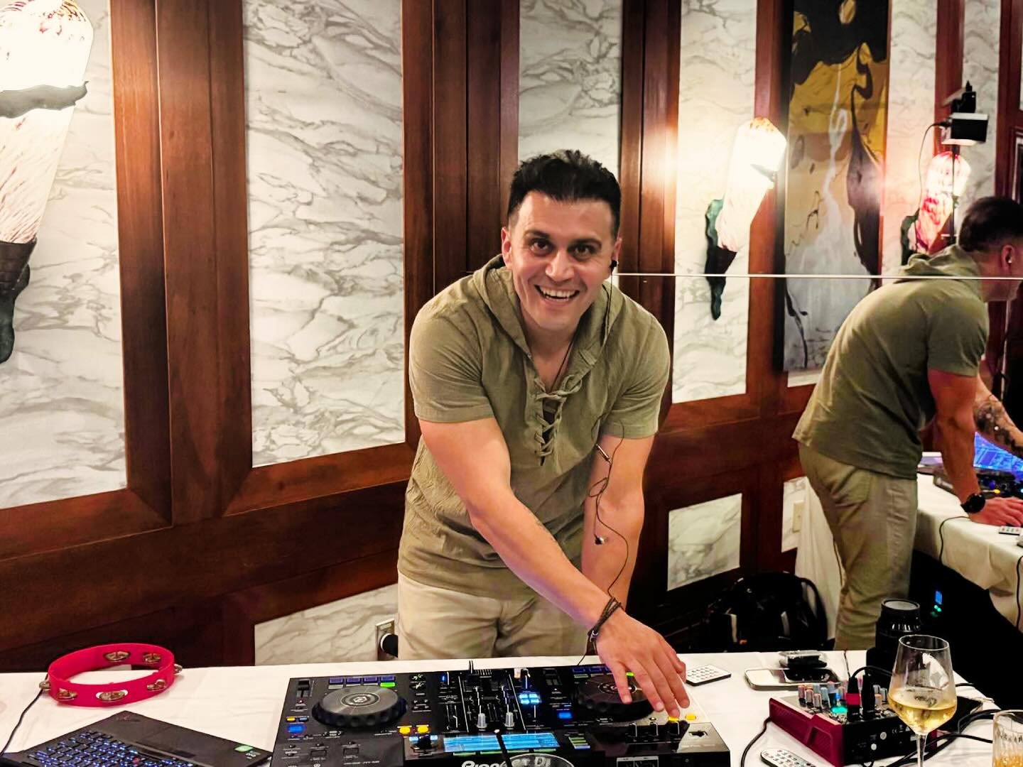 DJ Alphire smiling behind the decks on Pioneer DJ gear at an event.