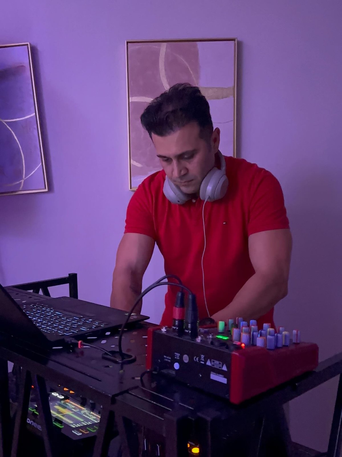 DJ Alphire mixing on DJ equipment with headphones around his neck