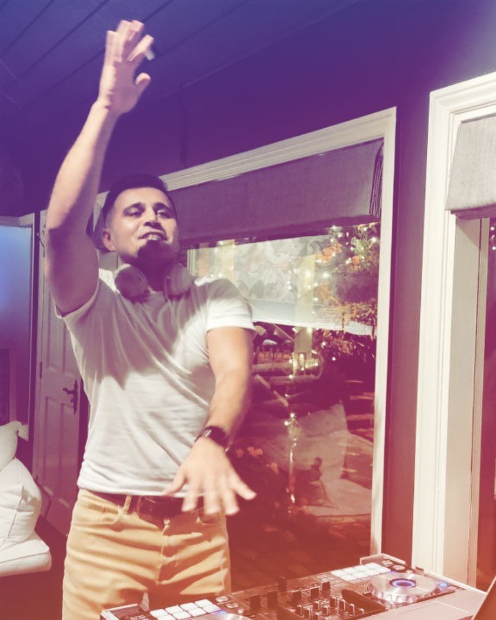 DJ Alphire performing on his DJ controller with arm raised at a party.